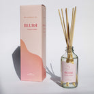 Diffuser bottle with 'Blush' label and packaging on a white background casting shadows in the sunlight.