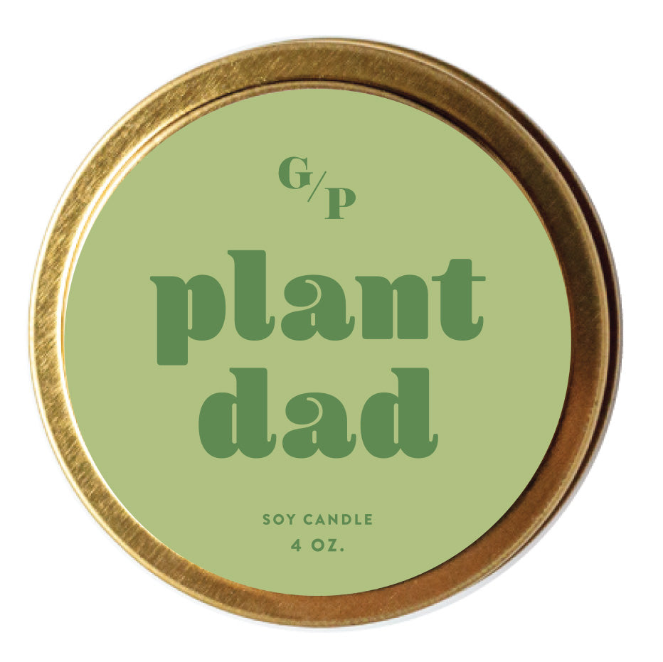 Top view of green candle tin lid with 'plant dad' text and gold rim.